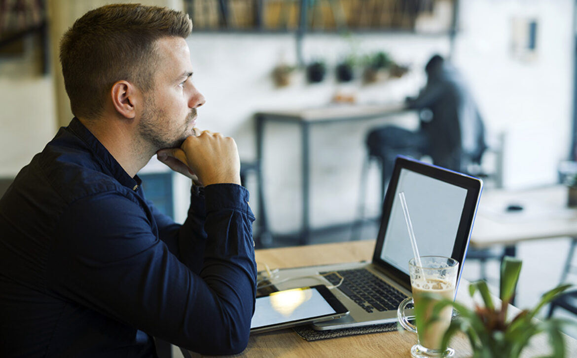 Young businessman sitting in cafe bar with laptop being worried